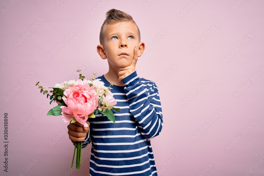 Young little caucasian kid holding romantic and cute bouquet of flowers over pink background serious face thinking about question, very confused idea Young little caucasian kid holding romantic and cute bouquet of flowers over pink background serious face thinking about question, very confused idea