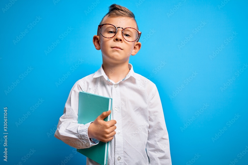 Young little caucasian student kid wearing smart glasses and holding a book from school with a confident expression on smart face thinking serious Young little caucasian student kid wearing smart glasses and holding a book from school with a confident expression on smart face thinking serious