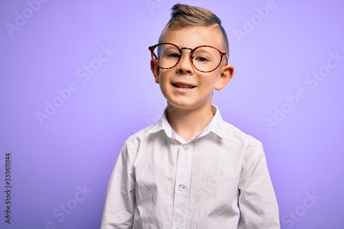 Young little caucasian kid with blue eyes wearing glasses and white shirt over purple background with a happy and cool smile on face. Lucky person.