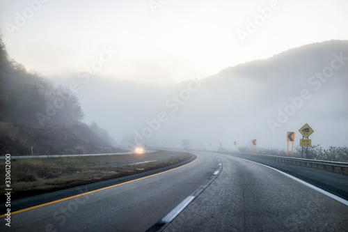 Foggy mist road highway driving with headlights in rural countryside in West Virginia with cars and entrance to clouds
