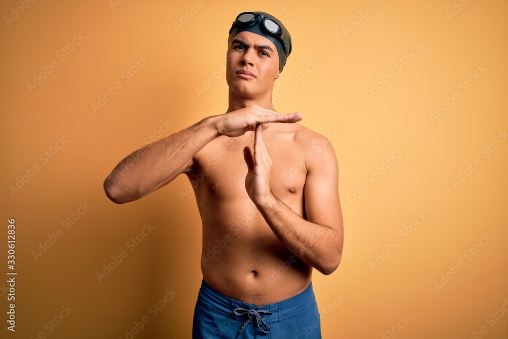 Young handsome man shirtless wearing swimsuit and swim cap over isolated yellow background Doing time out gesture with hands, frustrated and serious face
