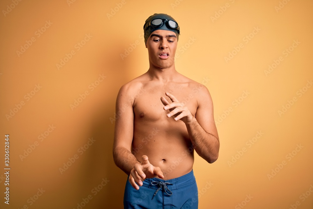 Young handsome man shirtless wearing swimsuit and swim cap over isolated yellow background disgusted expression, displeased and fearful doing disgust face because aversion reaction.