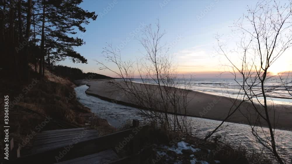 Sunset view from wooden walk path over Saulkrasti white dune. Fast current eiver in slow motion with sea in background Sunset view from wooden walk path over Saulkrasti white dune. Fast current eiver in slow motion with sea in background