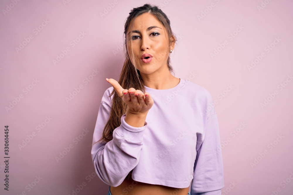 Young beautiful sport woman wearing sweatshirt over pink isolated background looking at the camera blowing a kiss with hand on air being lovely and sexy. Love expression. Young beautiful sport woman wearing sweatshirt over pink isolated background looking at the camera blowing a kiss with hand on air being lovely and sexy. Love expression.