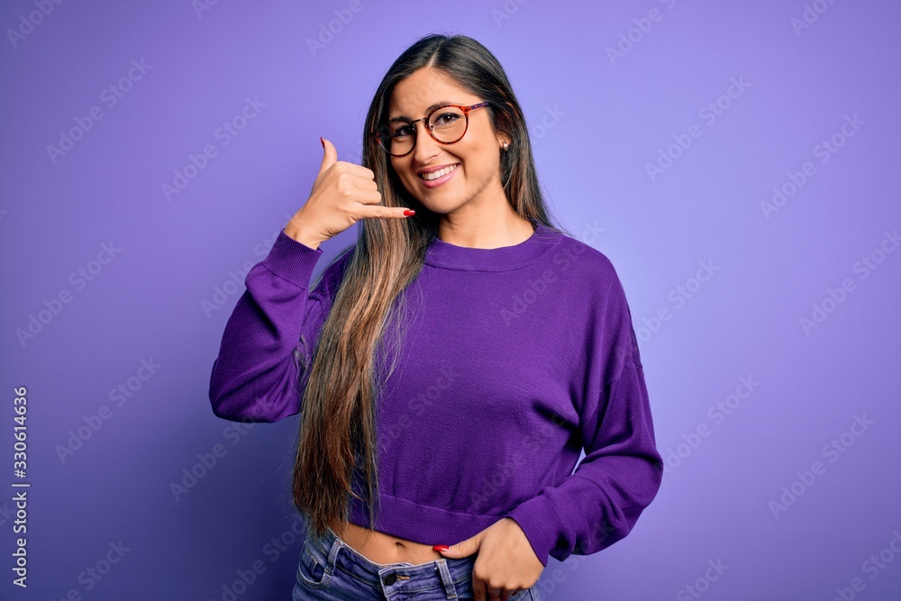 Young beautiful smart woman wearing glasses over purple isolated background smiling doing phone gesture with hand and fingers like talking on the telephone. Communicating concepts. Young beautiful smart woman wearing glasses over purple isolated background smiling doing phone gesture with hand and fingers like talking on the telephone. Communicating concepts.