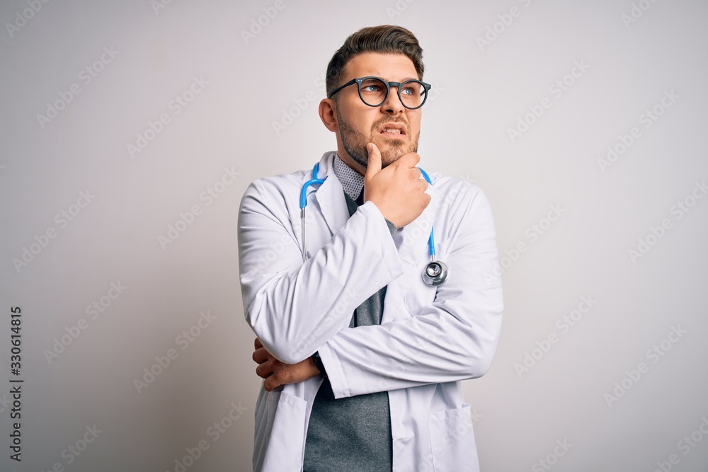 Young doctor man with blue eyes wearing medical coat and stethoscope over isolated background Thinking worried about a question, concerned and nervous with hand on chin Young doctor man with blue eyes wearing medical coat and stethoscope over isolated background Thinking worried about a question, concerned and nervous with hand on chin