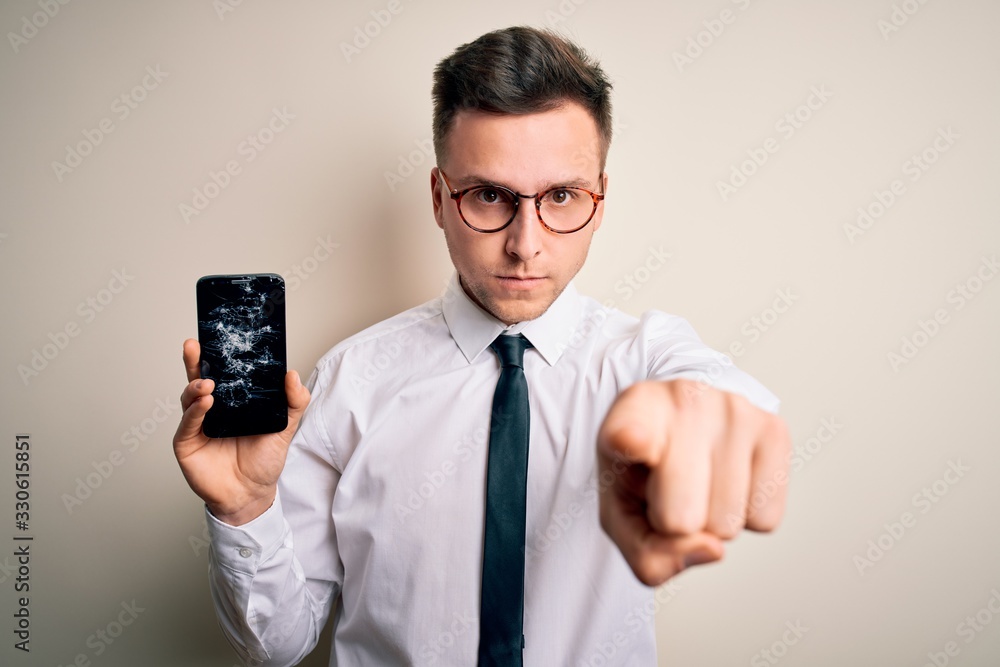 Young handsome caucasian man holding smartphone with broken screen over isolated background pointing with finger to the camera and to you, hand sign, positive and confident gesture from the front Young handsome caucasian man holding smartphone with broken screen over isolated background pointing with finger to the camera and to you, hand sign, positive and confident gesture from the front