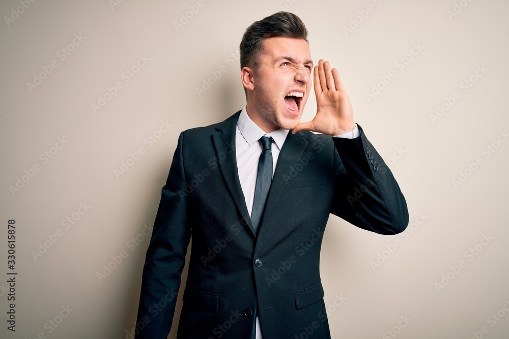 Young handsome business man wearing elegant suit and tie over isolated background shouting and screaming loud to side with hand on mouth. Communication concept. Young handsome business man wearing elegant suit and tie over isolated background shouting and screaming loud to side with hand on mouth. Communication concept.