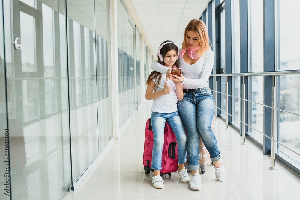 Happy young mother and her daughter walking in the airport terminal while carrying a suitcase. High season and vacation concept. Relax and lifestyles