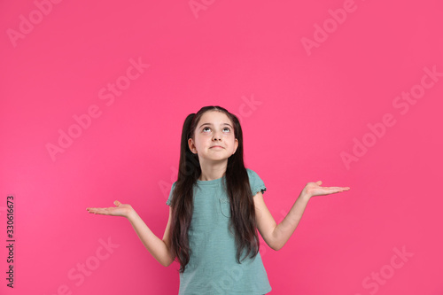 Portrait of confused little girl on pink background. Thinking about answer for question photo