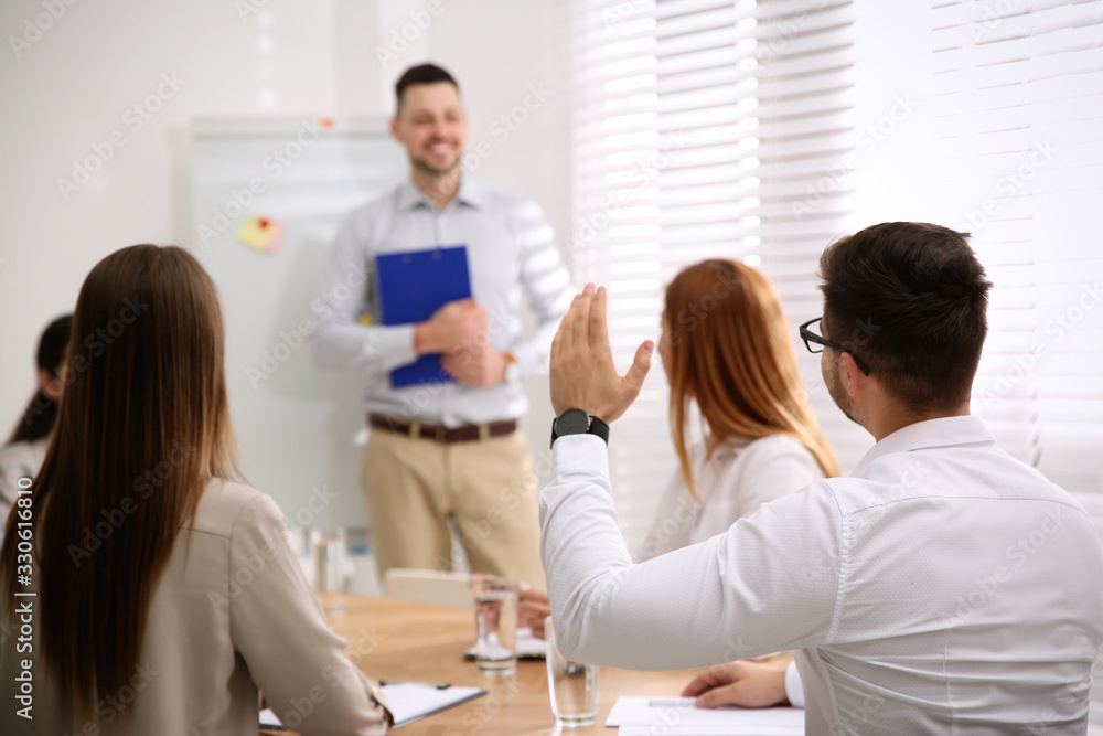 Young man raising hand to ask question at business training in conference room Young man raising hand to ask question at business training in conference room