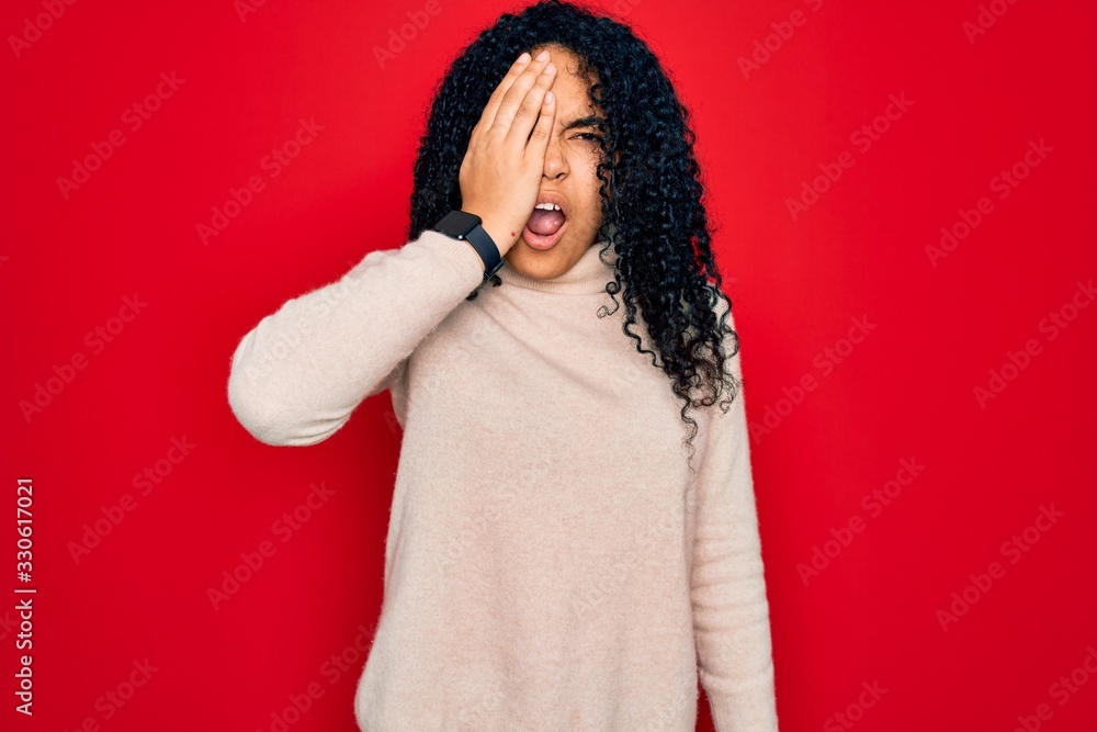 Young african american curly woman wearing casual turtleneck sweater over red background Yawning tired covering half face, eye and mouth with hand. Face hurts in pain. Young african american curly woman wearing casual turtleneck sweater over red background Yawning tired covering half face, eye and mouth with hand. Face hurts in pain.