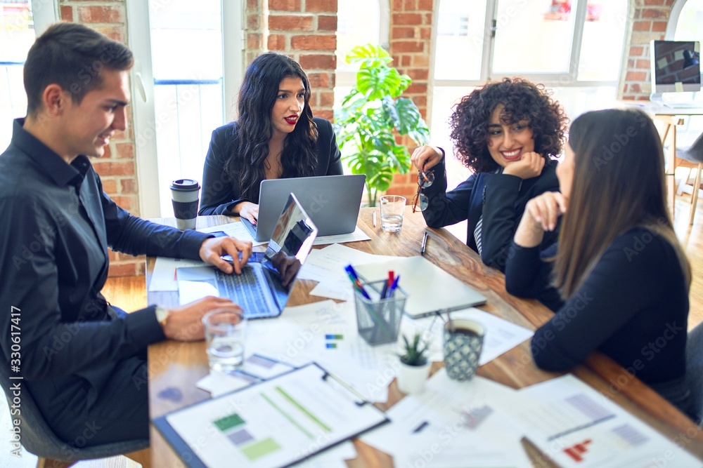 Group of business workers smiling happy and confident. Working together with smile on face using laptop and speaking at the office Group of business workers smiling happy and confident. Working together with smile on face using laptop and speaking at the office