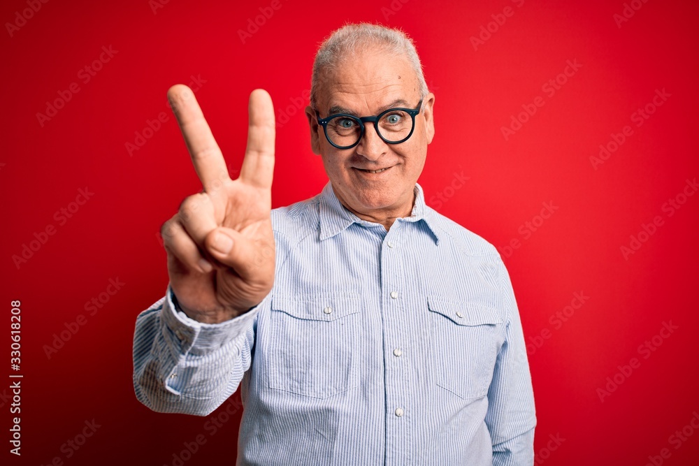 Middle age handsome hoary man wearing casual striped shirt and glasses over red background showing and pointing up with fingers number two while smiling confident and happy. Middle age handsome hoary man wearing casual striped shirt and glasses over red background showing and pointing up with fingers number two while smiling confident and happy.