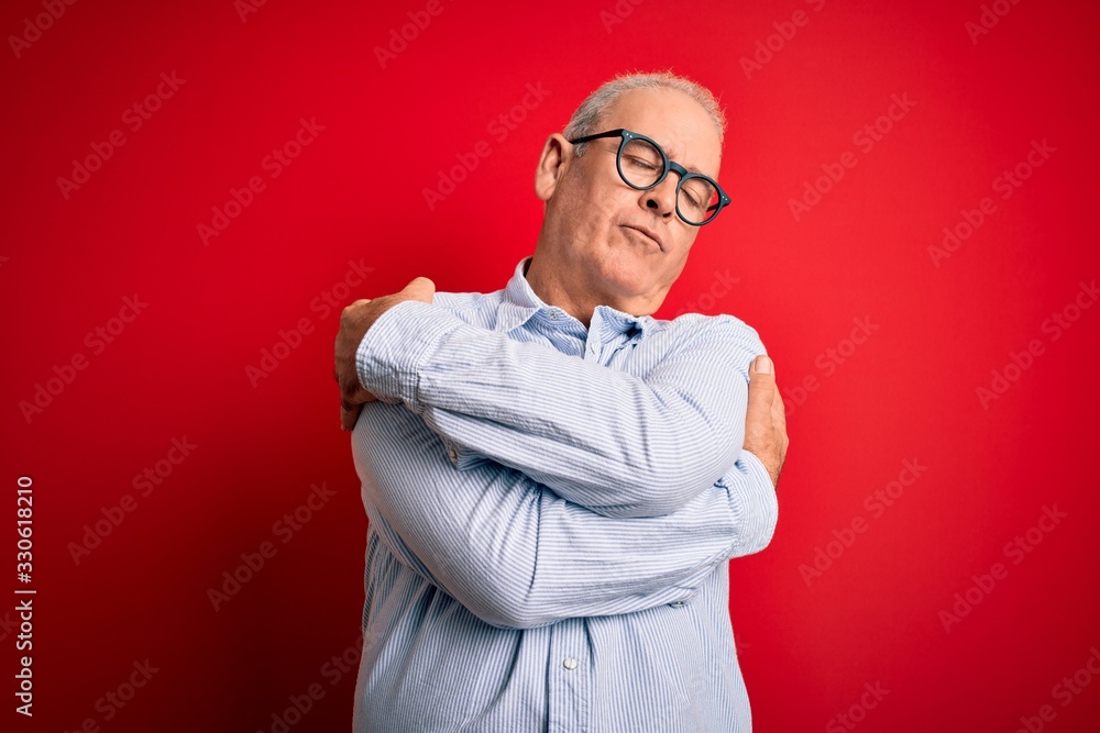 Middle age handsome hoary man wearing casual striped shirt and glasses over red background Hugging oneself happy and positive, smiling confident. Self love and self care Middle age handsome hoary man wearing casual striped shirt and glasses over red background Hugging oneself happy and positive, smiling confident. Self love and self care