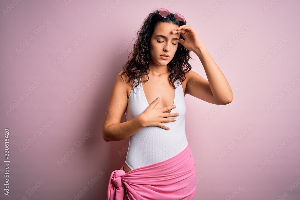 Beautiful woman with curly hair on vacation wearing white swimsuit over pink background Touching forehead for illness and fever, flu and cold, virus sick Beautiful woman with curly hair on vacation wearing white swimsuit over pink background Touching forehead for illness and fever, flu and cold, virus sick