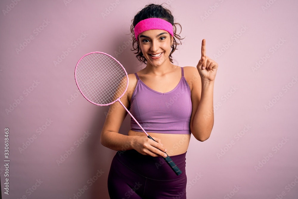 Beautiful sportswoman with curly hair wearing sportswear playing badminton uning racket surprised with an idea or question pointing finger with happy face, number one Beautiful sportswoman with curly hair wearing sportswear playing badminton uning racket surprised with an idea or question pointing finger with happy face, number one