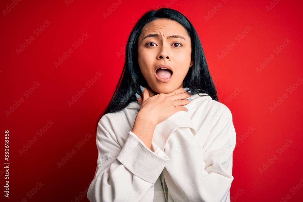 Young beautiful chinese sporty woman wearing sweatshirt over isolated red background shouting and suffocate because painful strangle. Health problem. Asphyxiate and suicide concept. Young beautiful chinese sporty woman wearing sweatshirt over isolated red background shouting and suffocate because painful strangle. Health problem. Asphyxiate and suicide concept.