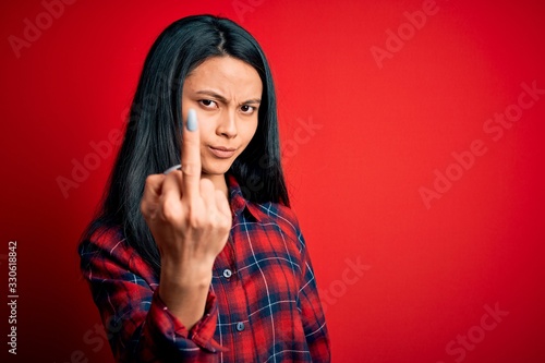 Young beautiful chinese woman wearing casual shirt over isolated red background Showing middle finger, impolite and rude fuck off expression © Krakenimages.com