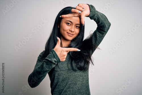 Young beautiful chinese woman wearing casual t-shirt over isolated white background smiling making frame with hands and fingers with happy face. Creativity and photography concept. © Krakenimages.com