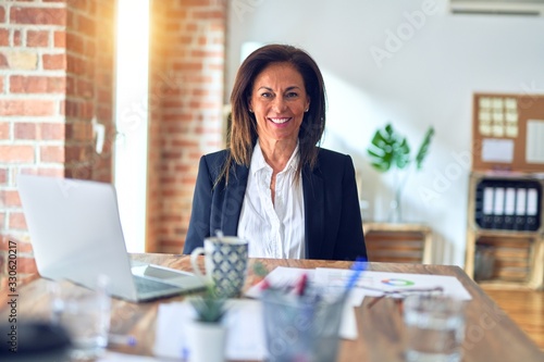 Middle age beautiful businesswoman working using laptop at the office with a happy and cool smile on face. Lucky person.