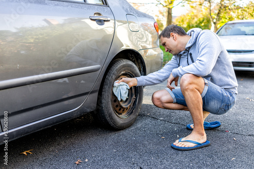 Person cleaning tire wheel with missing cap cover on parked car with man rubbing rusty hubcap with towel photo