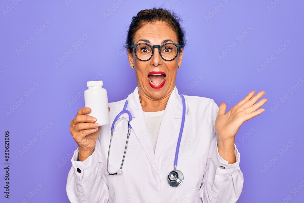 Middle age senior professional doctor woman holding pharmaceutical pills very happy and excited, winner expression celebrating victory screaming with big smile and raised hands Middle age senior professional doctor woman holding pharmaceutical pills very happy and excited, winner expression celebrating victory screaming with big smile and raised hands