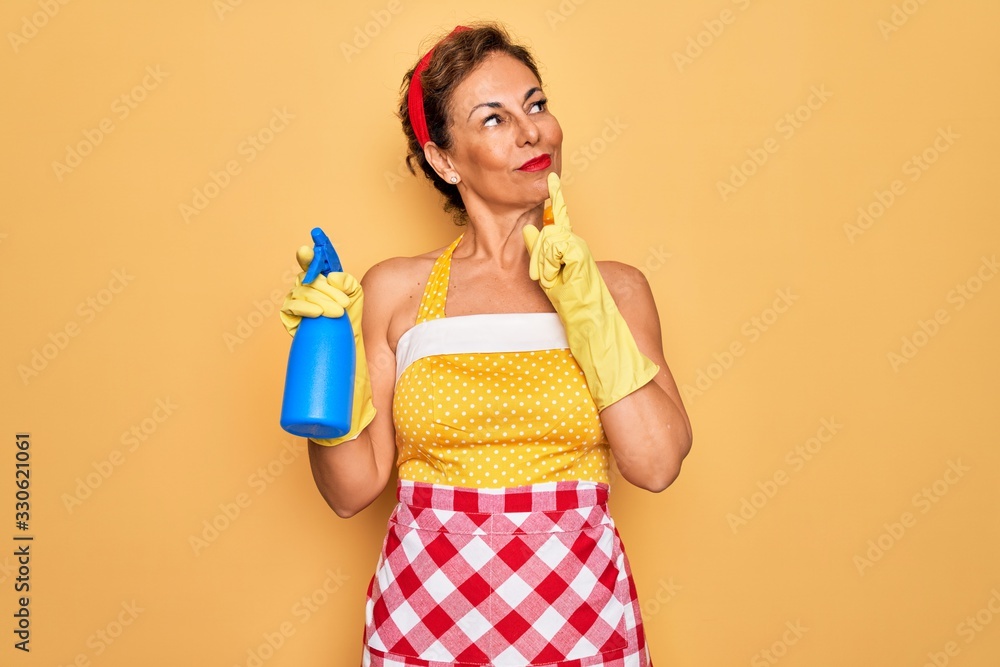 Middle age senior housewife pin up woman wearing 50s style retro dress cleaning using spray serious face thinking about question, very confused idea Middle age senior housewife pin up woman wearing 50s style retro dress cleaning using spray serious face thinking about question, very confused idea