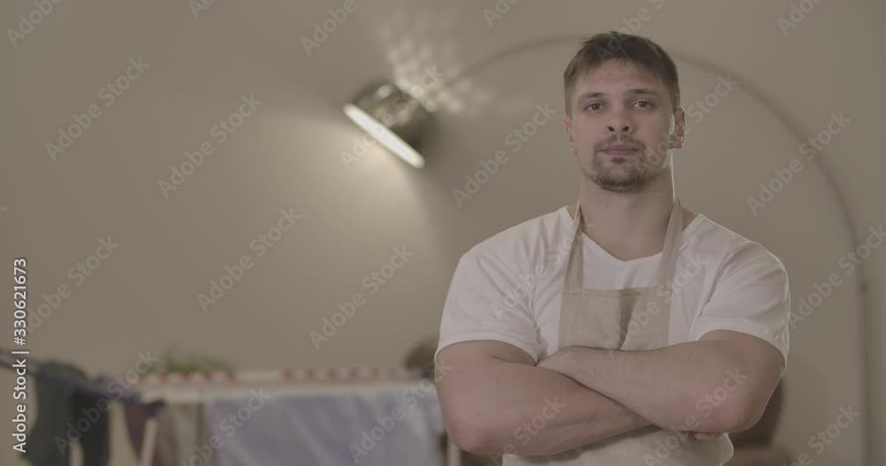 Brunette Caucasian man with brown eyes standing with hands crossed at the background of dryer indoors. Portrait of confident male housekeeper posing at home. Household. Cinema 4k ProRes HQ. Brunette Caucasian man with brown eyes standing with hands crossed at the background of dryer indoors. Portrait of confident male housekeeper posing at home. Household. Cinema 4k ProRes HQ.