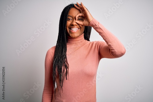 Young african american woman standing casual and cool over white isolated background doing ok gesture with hand smiling, eye looking through fingers with happy face.