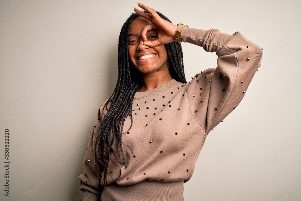 Fototapeta premium Young african american fashion woman standing casual over brown isolated background doing ok gesture with hand smiling, eye looking through fingers with happy face.