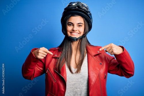 Young beautiful brunette motorcycliste woman wearing motorcycle helmet and jacket looking confident with smile on face, pointing oneself with fingers proud and happy. © Krakenimages.com