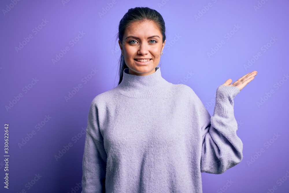 Young beautiful woman with blue eyes wearing casual turtleneck sweater over pink background smiling cheerful presenting and pointing with palm of hand looking at the camera. Young beautiful woman with blue eyes wearing casual turtleneck sweater over pink background smiling cheerful presenting and pointing with palm of hand looking at the camera.