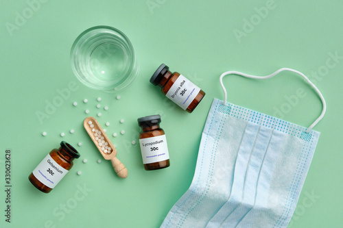 Bottles of homeopathic drugs - Gelsemium, Lycopodium, Bryonia - remedies recommended by homeopaths for treatment and prophylaxis of Coronavirus Covid-19, a glass of water, medical protective mask. photo