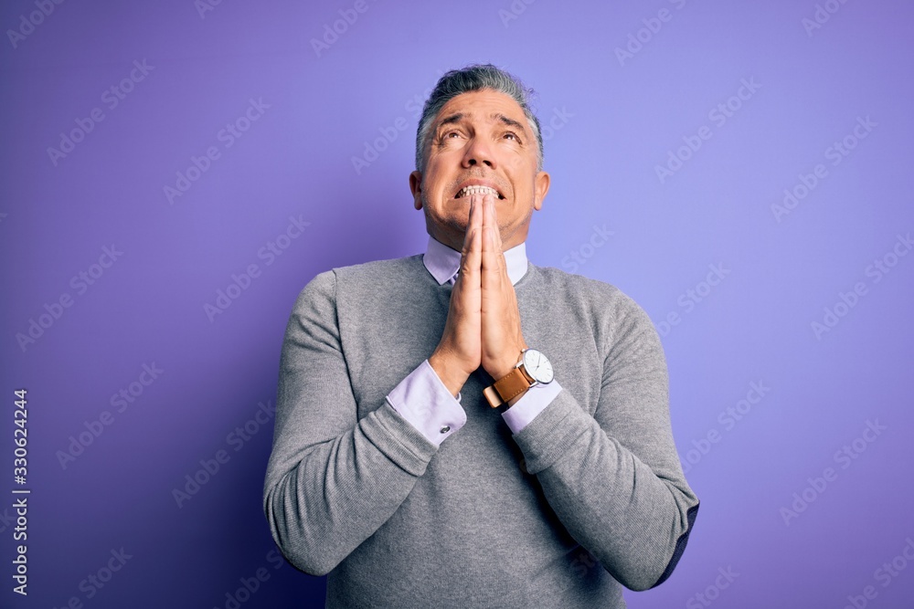 Middle age handsome grey-haired man wearing elegant sweater over purple background begging and praying with hands together with hope expression on face very emotional and worried. Begging. Middle age handsome grey-haired man wearing elegant sweater over purple background begging and praying with hands together with hope expression on face very emotional and worried. Begging.
