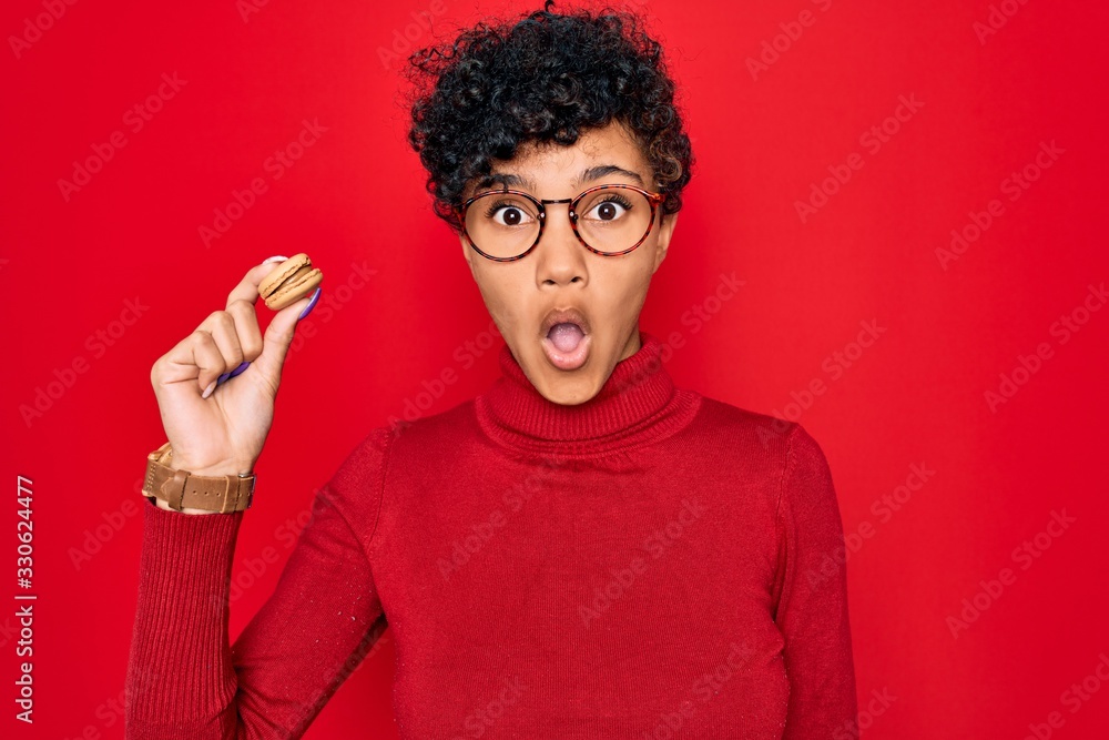 Young beautiful african american afro woman holding chocolate french dessert macaron scared in shock with a surprise face, afraid and excited with fear expression Young beautiful african american afro woman holding chocolate french dessert macaron scared in shock with a surprise face, afraid and excited with fear expression