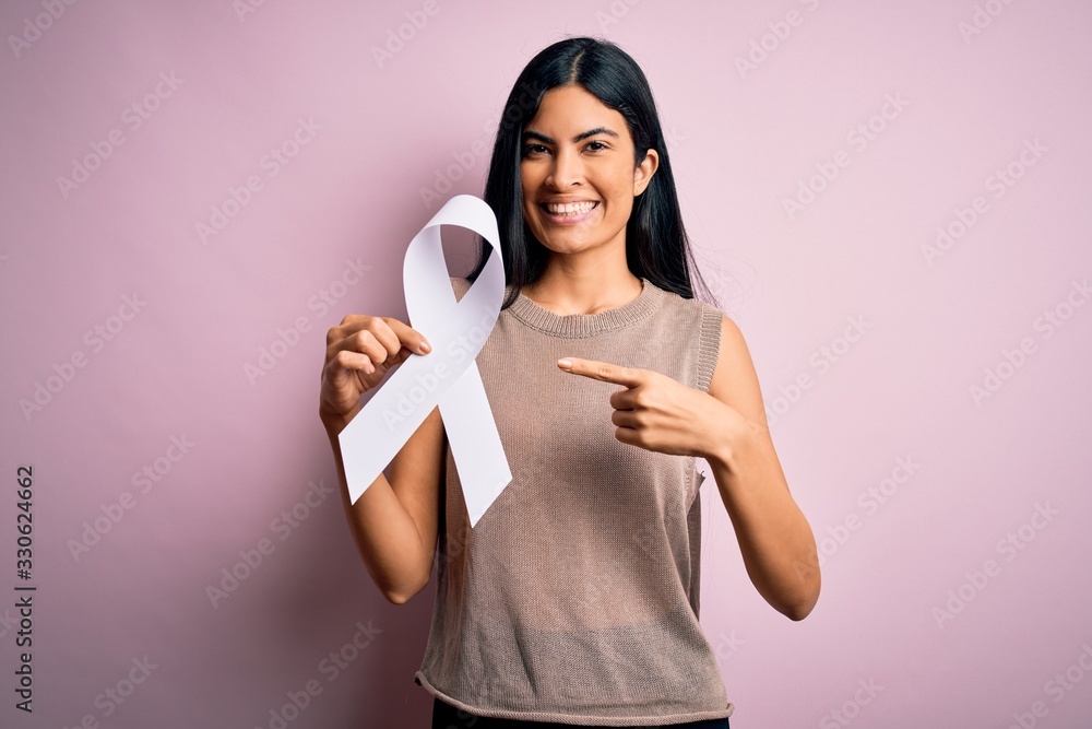 Young beautiful hispanic woman holding white ribbon as stop violence and lung cancer symbol very happy pointing with hand and finger Young beautiful hispanic woman holding white ribbon as stop violence and lung cancer symbol very happy pointing with hand and finger