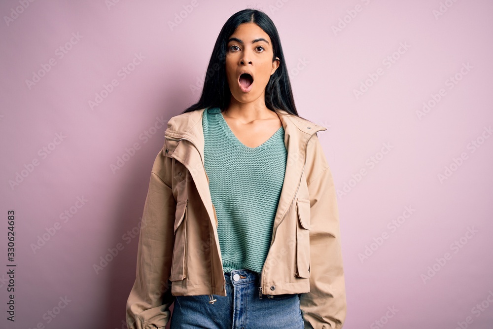 Young beautiful hispanic fashion woman wearing winter jacket and sweater over pink background afraid and shocked with surprise expression, fear and excited face. Young beautiful hispanic fashion woman wearing winter jacket and sweater over pink background afraid and shocked with surprise expression, fear and excited face.