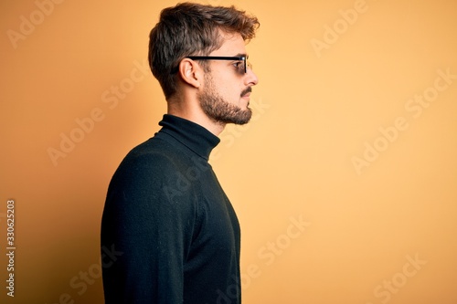 Young man wearing thug life fanny sunglasses standing over isolated yellow background looking to side, relax profile pose with natural face with confident smile.