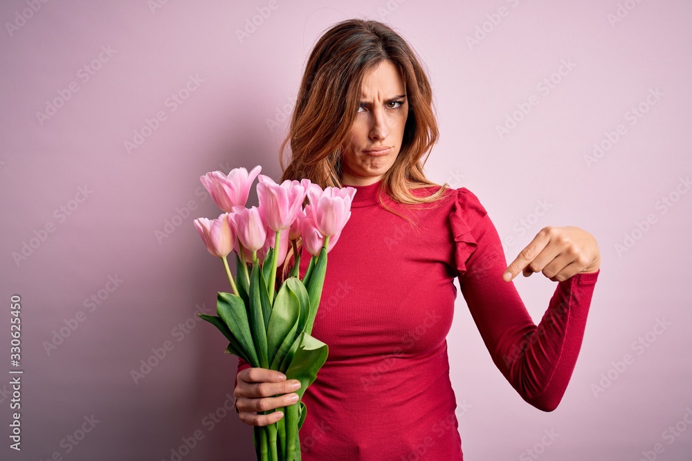 Young beautiful brunette woman holding bouquet of pink tulips over isolated background Pointing down looking sad and upset, indicating direction with fingers, unhappy and depressed. Young beautiful brunette woman holding bouquet of pink tulips over isolated background Pointing down looking sad and upset, indicating direction with fingers, unhappy and depressed.