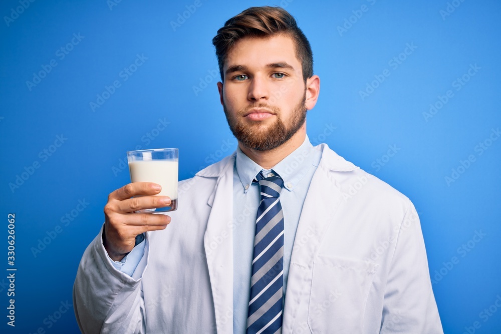 Young blond doctor man with beard and blue eyes wearing coat drinking glass of milk with a confident expression on smart face thinking serious Young blond doctor man with beard and blue eyes wearing coat drinking glass of milk with a confident expression on smart face thinking serious