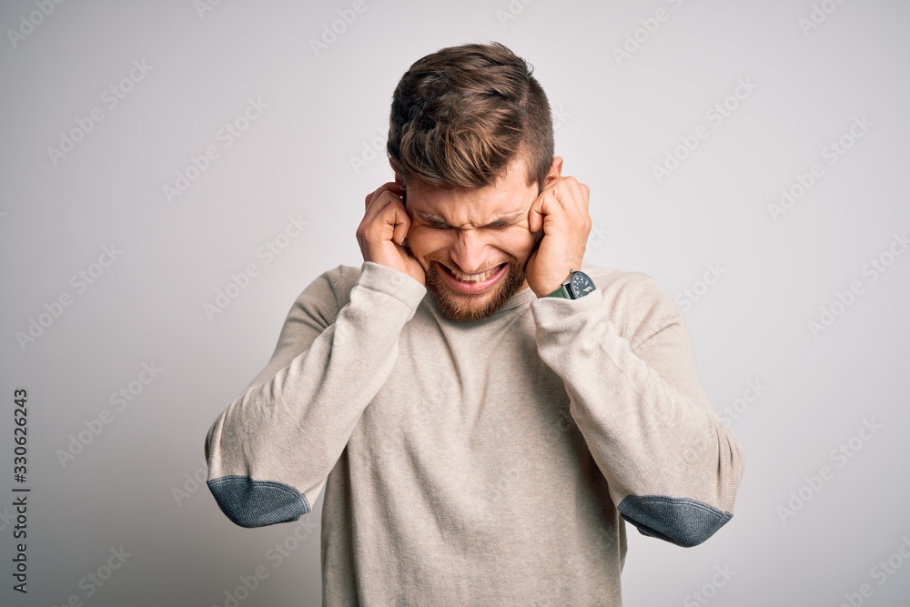 Young handsome blond man with beard and blue eyes wearing casual sweater covering ears with fingers with annoyed expression for the noise of loud music. Deaf concept. Young handsome blond man with beard and blue eyes wearing casual sweater covering ears with fingers with annoyed expression for the noise of loud music. Deaf concept.
