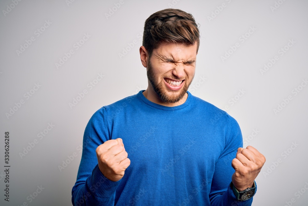 Young handsome blond man with beard and blue eyes wearing casual sweater very happy and excited doing winner gesture with arms raised, smiling and screaming for success. Celebration concept. Young handsome blond man with beard and blue eyes wearing casual sweater very happy and excited doing winner gesture with arms raised, smiling and screaming for success. Celebration concept.