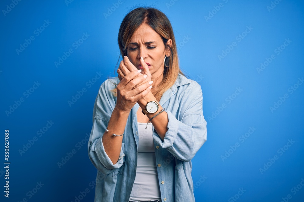 Middle age beautiful woman wearing casual shirt standing over isolated blue background Suffering pain on hands and fingers, arthritis inflammation Middle age beautiful woman wearing casual shirt standing over isolated blue background Suffering pain on hands and fingers, arthritis inflammation