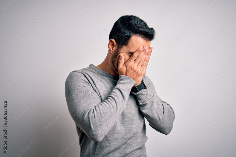 Young handsome man with beard wearing casual sweater standing over white background with sad expression covering face with hands while crying. Depression concept. Young handsome man with beard wearing casual sweater standing over white background with sad expression covering face with hands while crying. Depression concept.