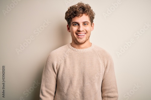 Young blond handsome man with curly hair wearing casual sweater over white background with a happy and cool smile on face. Lucky person.