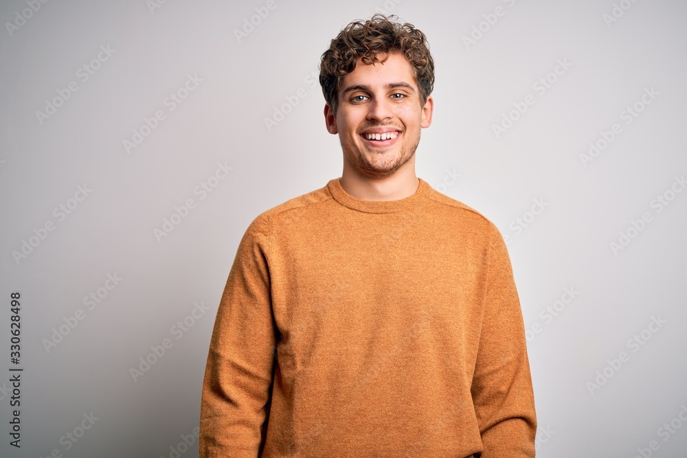 Young blond handsome man with curly hair wearing casual sweater over white background with a happy and cool smile on face. Lucky person. Young blond handsome man with curly hair wearing casual sweater over white background with a happy and cool smile on face. Lucky person.
