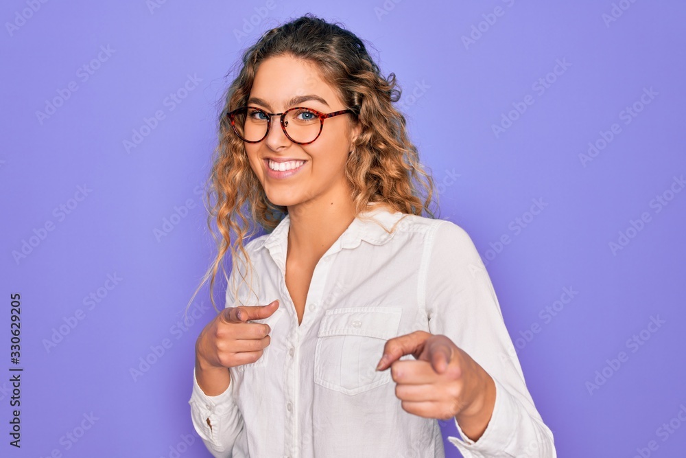 Young beautiful woman with blue eyes wearing casual shirt and glasses over purple background pointing fingers to camera with happy and funny face. Good energy and vibes. Young beautiful woman with blue eyes wearing casual shirt and glasses over purple background pointing fingers to camera with happy and funny face. Good energy and vibes.