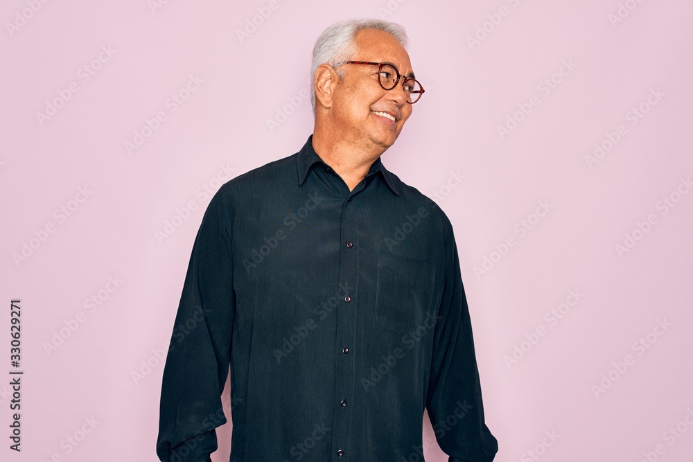 Middle age senior grey-haired handsome man wearing glasses and elegant shirt looking away to side with smile on face, natural expression. Laughing confident.