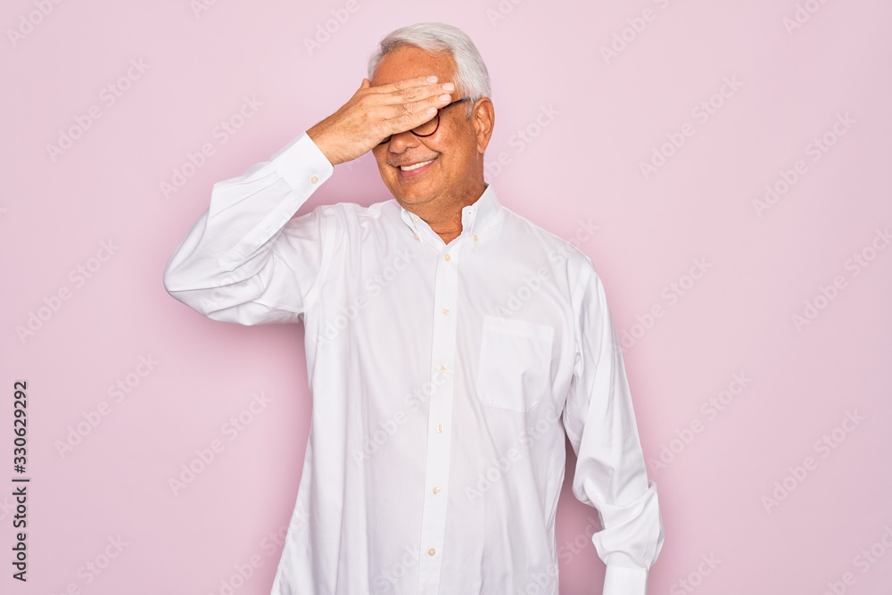 Middle age senior grey-haired man wearing glasses and business shirt over pink background smiling and laughing with hand on face covering eyes for surprise. Blind concept. Middle age senior grey-haired man wearing glasses and business shirt over pink background smiling and laughing with hand on face covering eyes for surprise. Blind concept.